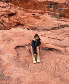 a woman sitting on top of a large rock next to a desert like area with rocks