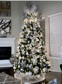 a decorated christmas tree in a living room with silver and white ornaments on the top