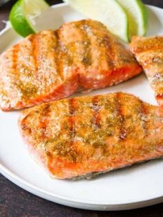 three pieces of salmon on a white plate with lime wedges next to the fish