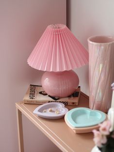 a pink lamp sitting on top of a wooden table next to a vase and plate