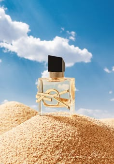 a bottle of perfume sitting on top of a pile of sand under a blue sky