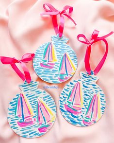 three sailboats painted on ceramic ornaments tied with pink ribbons and bows are sitting on a bed