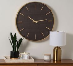 a large clock on the wall above a table with a lamp and potted plant