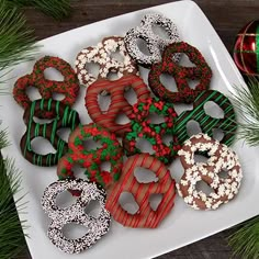 a white plate topped with lots of decorated donuts next to christmas tree branches and ornaments