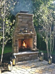 an outdoor fireplace in the middle of a yard with trees and bushes around it, lit by lanterns