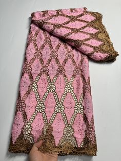 a pink and brown scarf being held up by a person's hand on a white surface