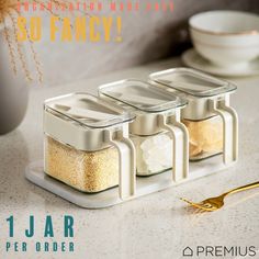 three salt and pepper shakers sitting on a counter top next to a gold spoon