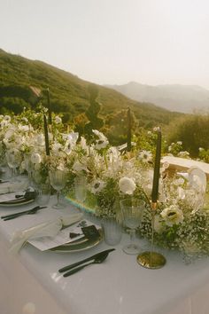 a long table with white flowers and black utensils is set up for an outdoor dinner