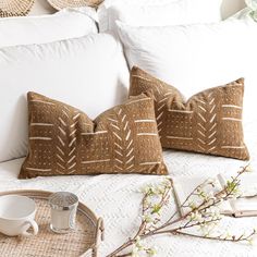 two decorative pillows sitting on top of a bed next to a cup and saucer