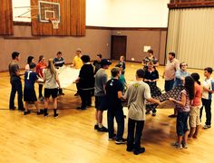 a group of people standing around in a gym with a basketball hoop on the wall