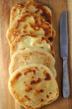 four flat breads sitting on top of a wooden cutting board next to a knife