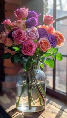 a vase filled with pink and purple roses on top of a wooden table next to a window