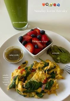 a white plate topped with eggs and fruit next to a cup of green smoothie