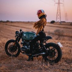 a woman sitting on top of a motorcycle in the middle of a field with power lines behind her