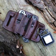 a cell phone is sitting in a leather case next to a keychain on a tree trunk