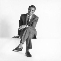 a black and white photo of a man in a suit sitting on a ledge with his legs crossed