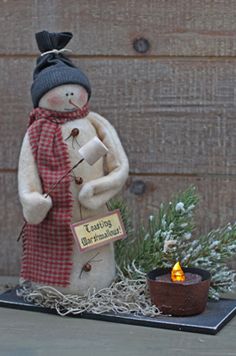 a snowman with a hat and scarf holding a lit candle in front of a building