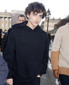 a young man is walking down the street with his hands in his pockets and wearing a black hoodie