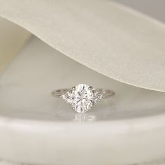 a diamond engagement ring sitting on top of a white cloth covered table with a satin bow