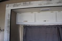 the inside of a bathroom with white cabinets and gray curtains