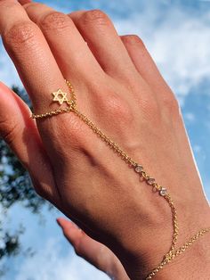 14 Karat Gold Filled CZ Hand Chain with our mini Star of David charm dangling by the ring finger. Bracelet length:  6" + .5" Extension Finger Loop: 2.5"  Hand Chain Piece: 3.75" Material: 18 Karat Gold Filled, Hypoallergenic. Tarnish Resistant. Gold-filled does not de-laminate or peel like Gold plated Jewelry nor does it tarnish as readily as silver. Generally speaking, gold filled is better quality and will have a much longer lasting color than plated jewelry. Gold filled jewelry is an excellent option for those who wish to have a product of exceptional quality, beautiful and anti-allergenic, but with prices far lower than solid gold jewelry. We recommend keeping abrasive chemicals away from the jewelry for the items to last. Thank you for visiting and supporting our small business! We ho David Ring, Hand Chain Bracelet, Dainty Style, Tiny Star, Alessandra Ambrosio, Hand Chain, Vanessa Hudgens, Solid Gold Jewelry, Hand Jewelry