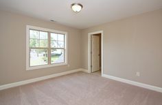 an empty room with a door and window on the far wall, carpeted floor