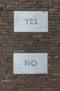 two signs on a brick wall that say yes and no