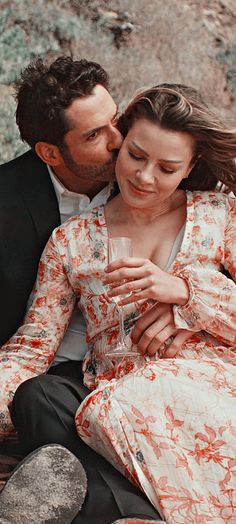 a man and woman sitting next to each other on the ground with wine glasses in their hands