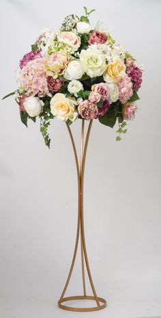 a vase filled with lots of flowers on top of a metal stand in front of a white wall