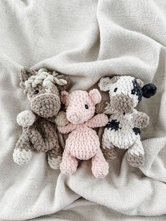 three crocheted stuffed animals laying on top of a white cloth covered in blankets