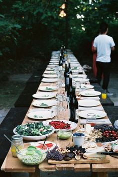 a long table is set up with plates and bowls of food on it, while a man stands in the background