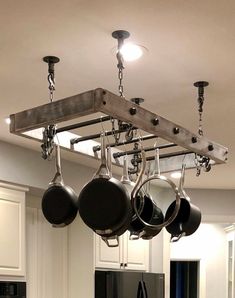 pots and pans are hanging from the ceiling in a kitchen with white cabinets, black appliances