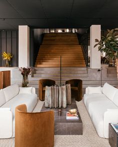 a living room filled with white couches next to a stair case and wooden table