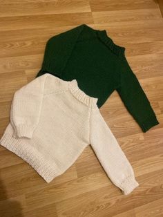 two sweaters laying on the floor next to each other, one green and one white