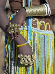 a woman in an african dress with gold bracelets and rings on her arm, holding onto the other side of her waist