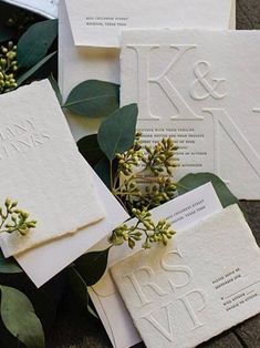 wedding stationery and envelopes with greenery on the ground next to each other