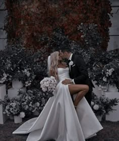 a bride and groom are kissing in front of some potted plants with white flowers