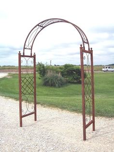 two metal archways sitting on top of a gravel road next to a lush green field