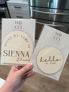 two personalized wooden coasters are being held up in front of the kitchen counter