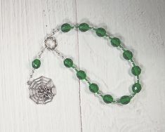 "This set of Mokosh prayer beads consists of a loop of twelve beads; joining the string is an additional bead and a pendant, a symbol representing the goddess: a spider's web, a reminder of her role as goddess of spinning and weaving. It is made with 10mm deep green fire-polished glass beads, separated by silver-toned metal spacer beads, and glass seed beads to provide a comfortable transition from one bead to the next and to make the piece lightweight, supple, and easy to handle. The string its Faceted Spiritual Beads For Gifts, Adjustable Spiritual Rosary With Spacer Beads, Adjustable Rosary With Oval Beads As Gift, Hand-strung Round Beads Rosary As A Gift, Hand-strung Rosary With Round Beads As Gift, Spiritual Rosary With Spacer Beads, Spiritual Rosary Bracelet With Round Beads As Gift, Hand-strung Rosary As A Gift, Spiritual Rosary Bracelet With Polished Beads