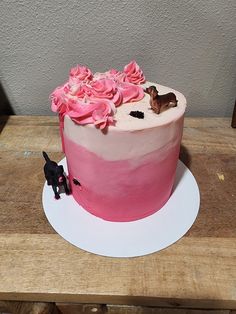 a pink cake with white frosting and flowers on the top is sitting on a wooden table