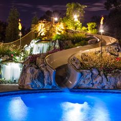 a pool with a slide in the middle and landscaping around it at night, lit up by street lights