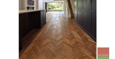 a long hallway with wood floors and black cabinets on both sides, leading to an open kitchen