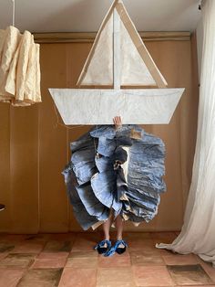 a person standing in front of a sailboat made out of blue jeans and paper