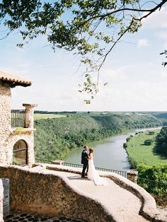 a bride and groom standing on top of a hill overlooking a river in the distance