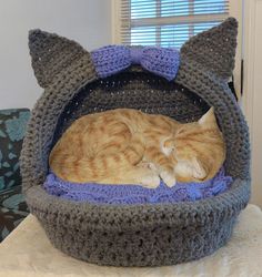 an orange cat sleeping in a crocheted kitty bed on top of a table