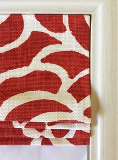 a red and white patterned curtain hanging in front of a window with a wooden frame