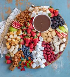 a platter filled with fruit, crackers, and chocolate sauce on top of a blue table