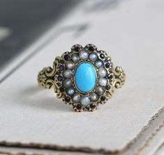 "Circa 1820 an antique Georgian turquoise and pearl halo ring in exquisite condition crafted in 14k gold with a rich buttery glow. Featuring a bright turquoise paste center stone surrounded by natural pearls and tiny faceted jet; such a rare piece, it epitomizes all the romantic charm of the Regency era. Measuring approximately 7/16\" north to south at the center front, tapering through to 2.37 mm at the center back. Size 6 1/4, resizing is not recommended. Paste is essentially a tyoe of leaded Victorian Turquoise Jewelry For Anniversary, Turquoise Victorian Jewelry For Anniversary, Antique Round Turquoise Wedding Ring, Antique Turquoise Round Ring For Wedding, Antique Turquoise Ring For Wedding, Victorian Turquoise Gemstone Jewelry, Antique Oval Turquoise Wedding Ring, Antique Style Turquoise Wedding Ring With Cabochon, Antique Oval Turquoise Ring For Wedding