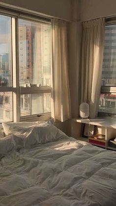 an unmade bed in front of large windows with cityscape outside the window